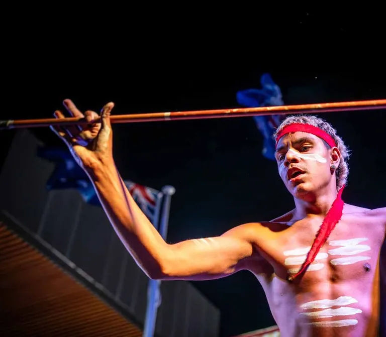 An Aboriginal dancer performing after dark with a boomerang and spear, body painted in white ochre