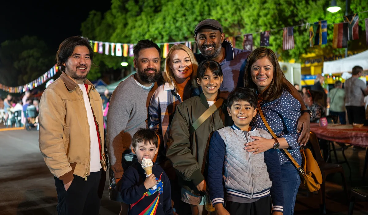 A multigenerational family group smiling together beneath international flags at One Long Table