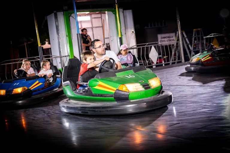 A dad and his young son driving a green bumper car at the free kids area at night