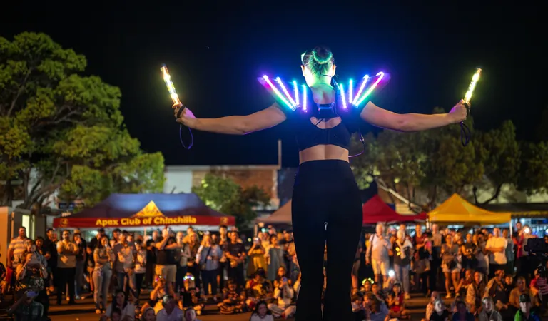 An LED performer holding illuminated batons before the festival crowd after dark