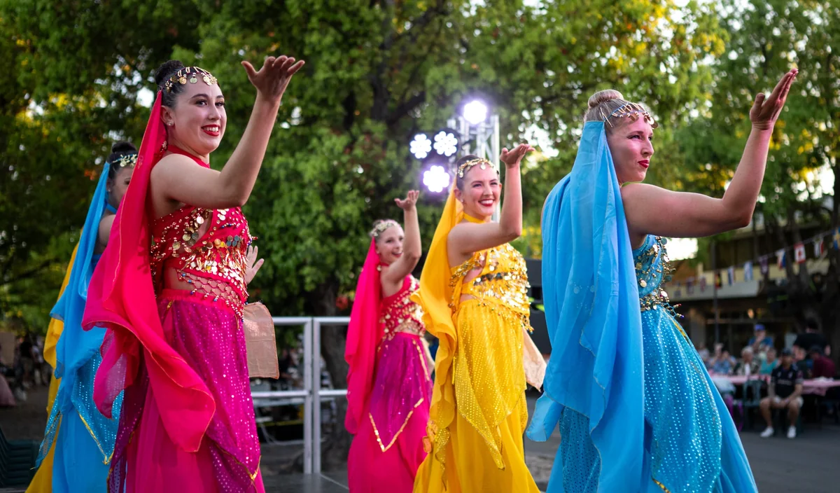 Three dancers in bright pink, yellow and blue costumes performing in the street