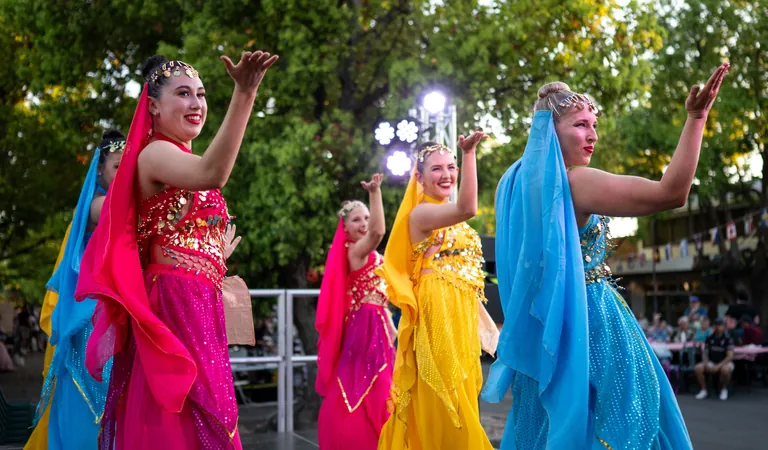 Three dancers in bright pink, yellow and blue costumes performing in the street